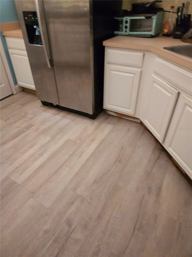 interior space with white cabinetry, light hardwood / wood-style floors, sink, and stainless steel fridge