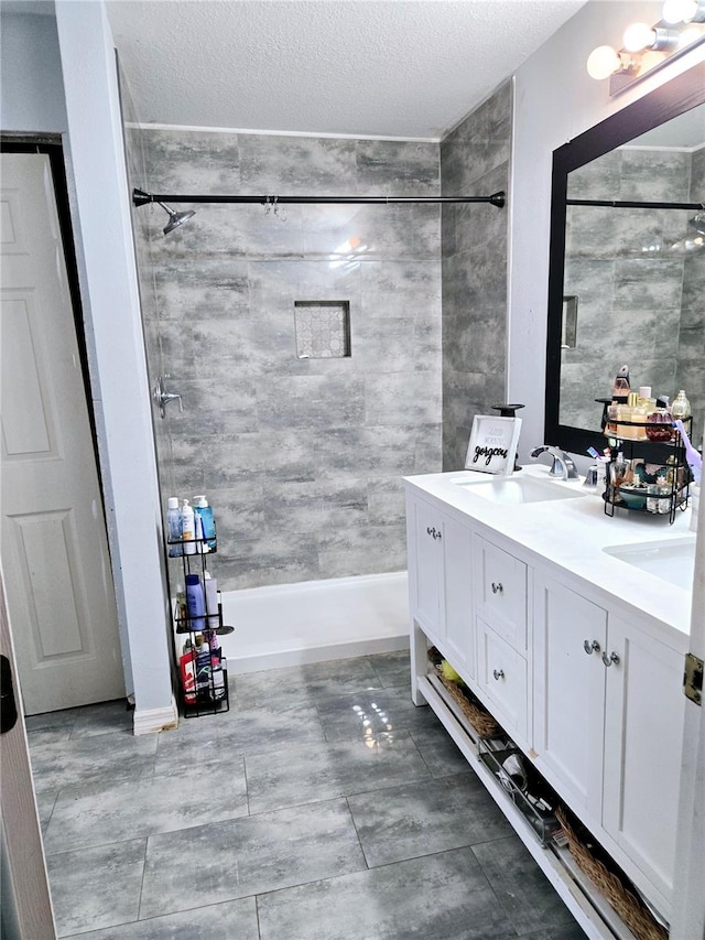 bathroom featuring a textured ceiling, vanity, and tiled shower