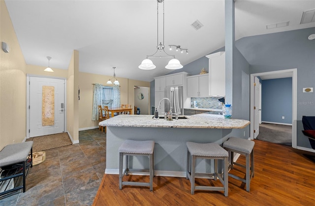 kitchen with a breakfast bar area, vaulted ceiling, white cabinetry, decorative light fixtures, and dark hardwood / wood-style flooring