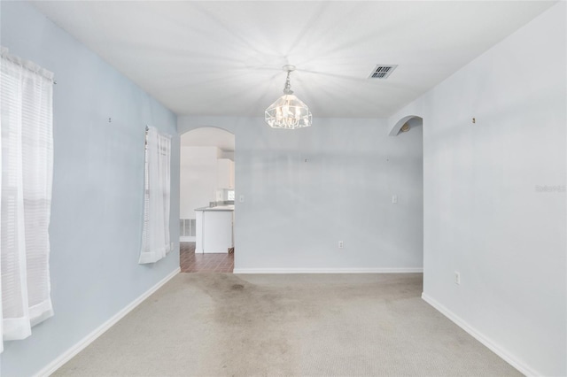 carpeted empty room featuring an inviting chandelier