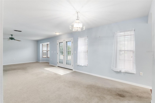 carpeted spare room featuring ceiling fan with notable chandelier and french doors