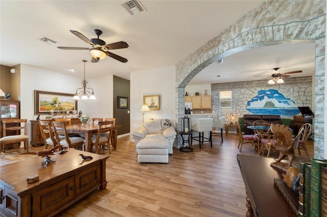 living room with ceiling fan with notable chandelier, light wood-type flooring, and a textured ceiling