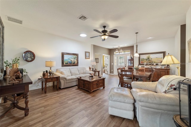 living room featuring ceiling fan with notable chandelier and light hardwood / wood-style flooring