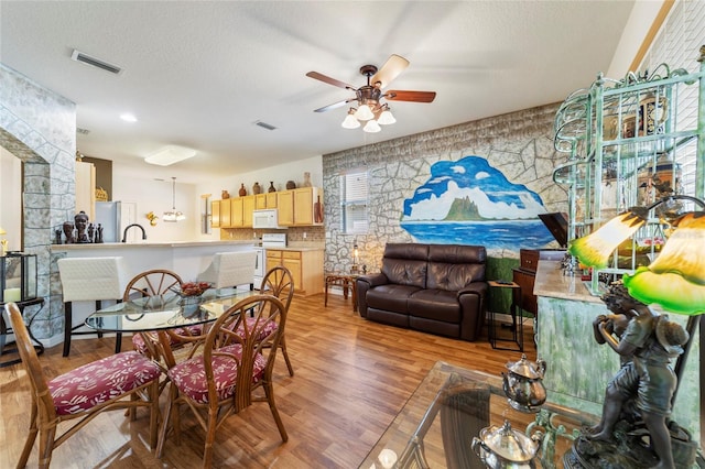 dining space featuring light wood-type flooring, a textured ceiling, sink, and ceiling fan