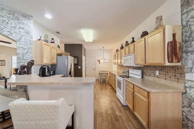 kitchen featuring light hardwood / wood-style floors, kitchen peninsula, a kitchen breakfast bar, white appliances, and light brown cabinetry