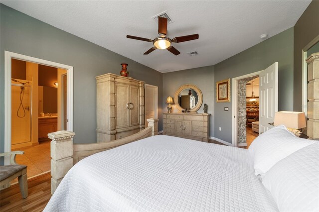 bedroom with ceiling fan, a textured ceiling, light hardwood / wood-style floors, and ensuite bathroom