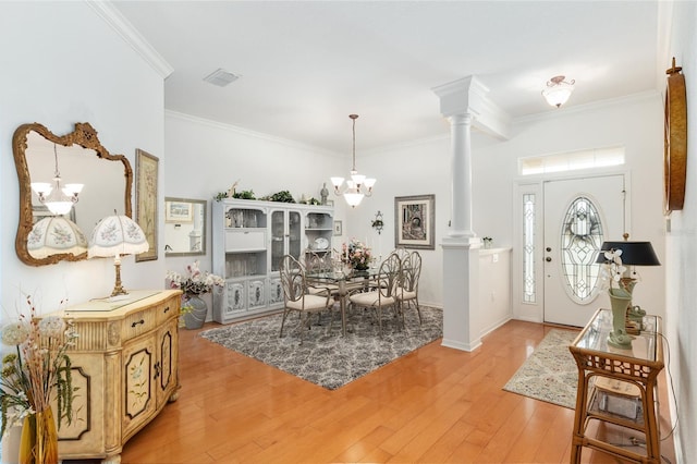 entrance foyer featuring ornate columns, ornamental molding, an inviting chandelier, and hardwood / wood-style flooring