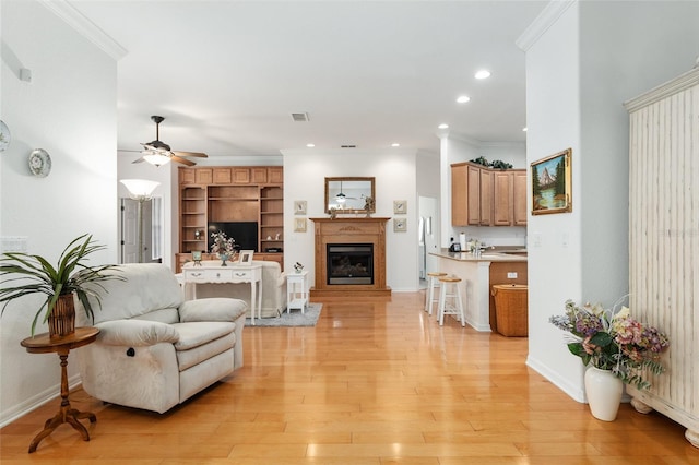 living room with light hardwood / wood-style flooring, built in shelves, ceiling fan, and crown molding