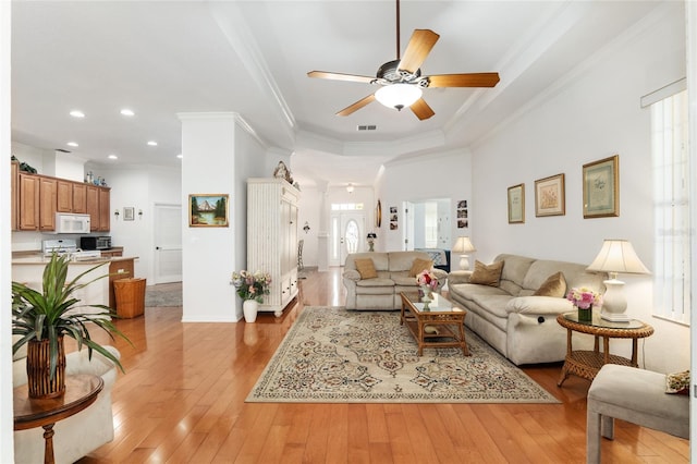 living room featuring light wood-type flooring, a healthy amount of sunlight, ornamental molding, and ceiling fan