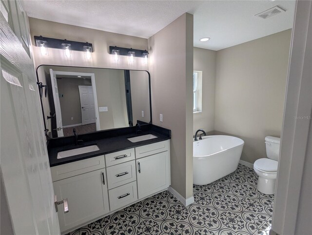 bathroom with vanity, a bathing tub, tile patterned flooring, toilet, and a textured ceiling