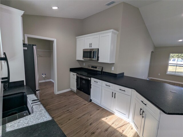 kitchen with white cabinets, appliances with stainless steel finishes, light wood-type flooring, and lofted ceiling