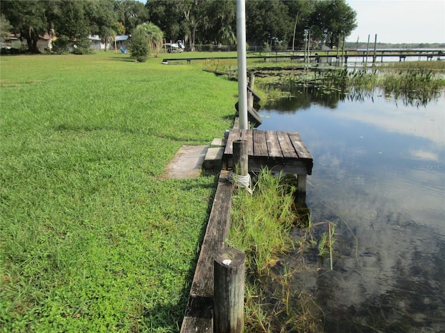 view of dock featuring a lawn and a water view