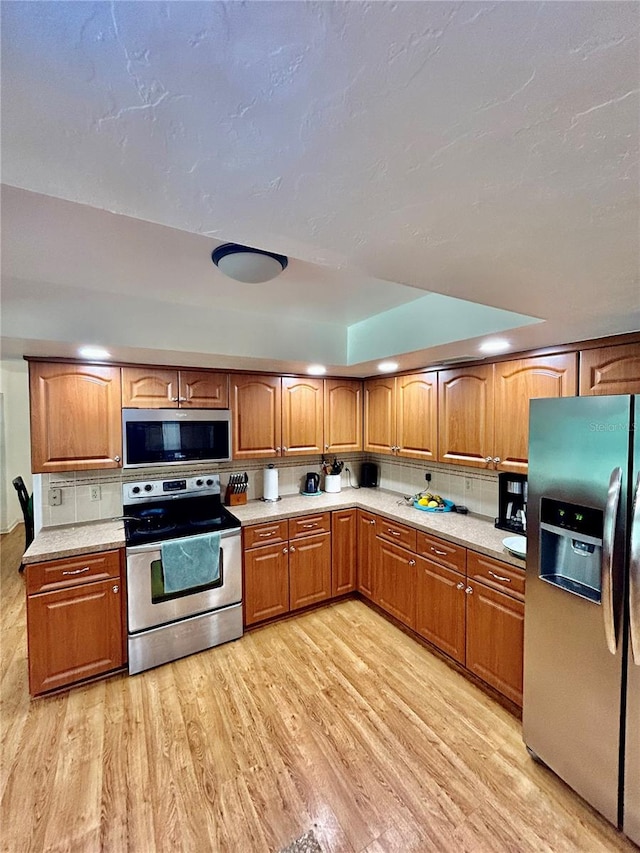 kitchen featuring light wood-type flooring, stainless steel appliances, and tasteful backsplash