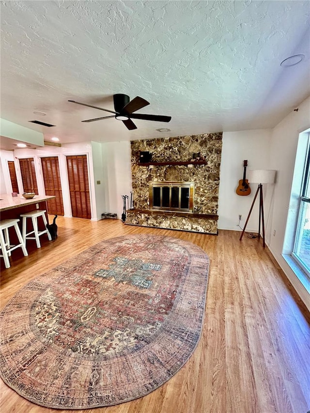 living room with a stone fireplace, ceiling fan, hardwood / wood-style floors, and a textured ceiling