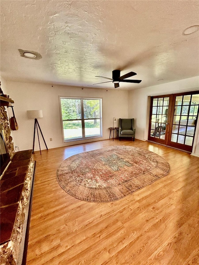 unfurnished living room featuring hardwood / wood-style floors, a textured ceiling, a stone fireplace, and ceiling fan