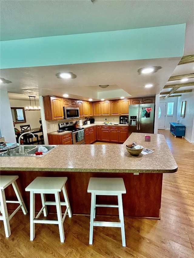 kitchen featuring sink, light wood-type flooring, a kitchen bar, kitchen peninsula, and stainless steel appliances