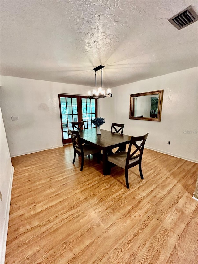 dining room with light hardwood / wood-style floors, a textured ceiling, and an inviting chandelier