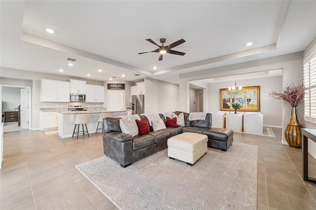 living room featuring ceiling fan with notable chandelier, a raised ceiling, and light tile patterned floors