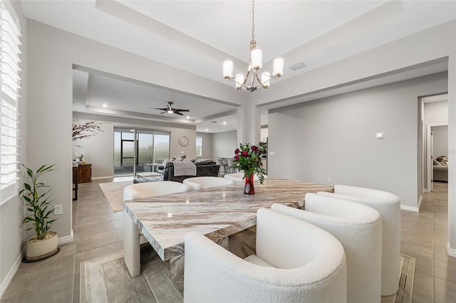 dining area featuring ceiling fan with notable chandelier, light tile patterned floors, and a tray ceiling