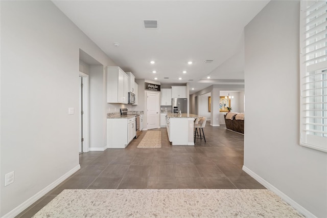 kitchen featuring light stone countertops, a kitchen breakfast bar, a center island with sink, white cabinets, and appliances with stainless steel finishes