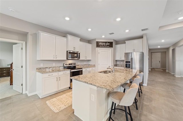 kitchen featuring stainless steel appliances, white cabinetry, a kitchen island with sink, and sink