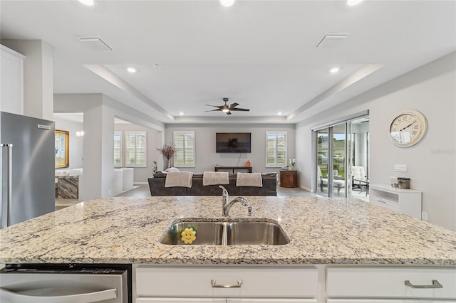 kitchen featuring ceiling fan, sink, a raised ceiling, light stone counters, and white cabinets