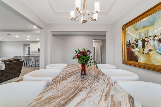 dining space featuring a raised ceiling, light hardwood / wood-style floors, and a notable chandelier