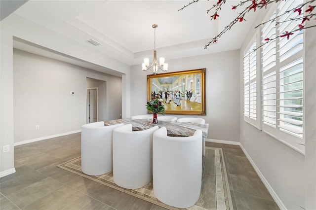 dining area featuring a raised ceiling, a chandelier, and dark tile patterned flooring