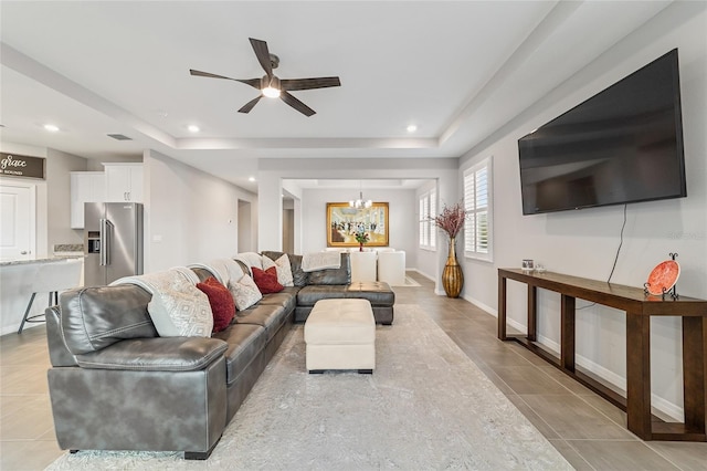 living room featuring ceiling fan with notable chandelier, a raised ceiling, and light tile patterned flooring