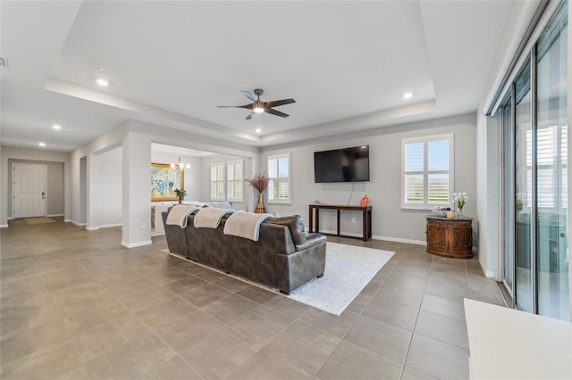 living room featuring a raised ceiling, a wealth of natural light, and ceiling fan with notable chandelier