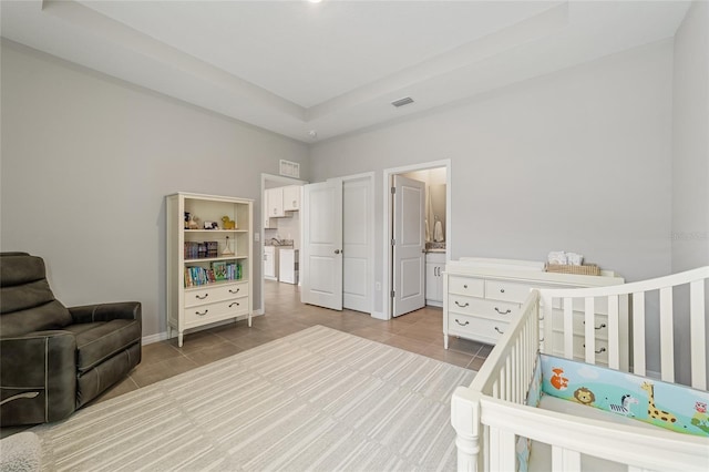 bedroom with tile patterned floors, a raised ceiling, ensuite bath, and a crib