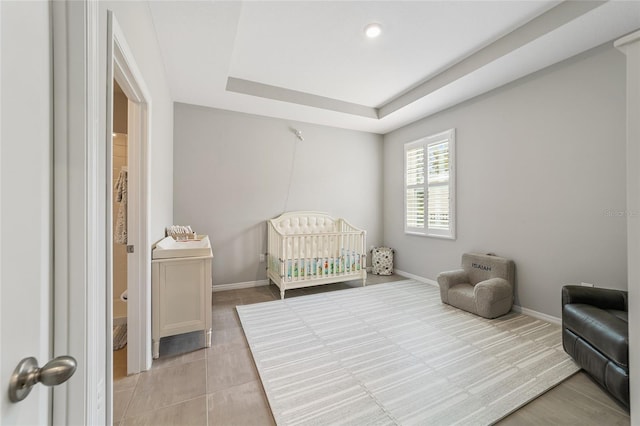 bedroom featuring a crib, light tile patterned floors, and a tray ceiling