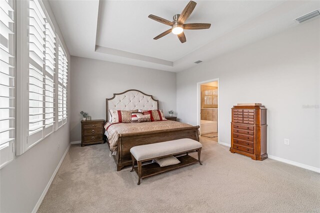 bedroom with light carpet, a tray ceiling, ensuite bath, and ceiling fan