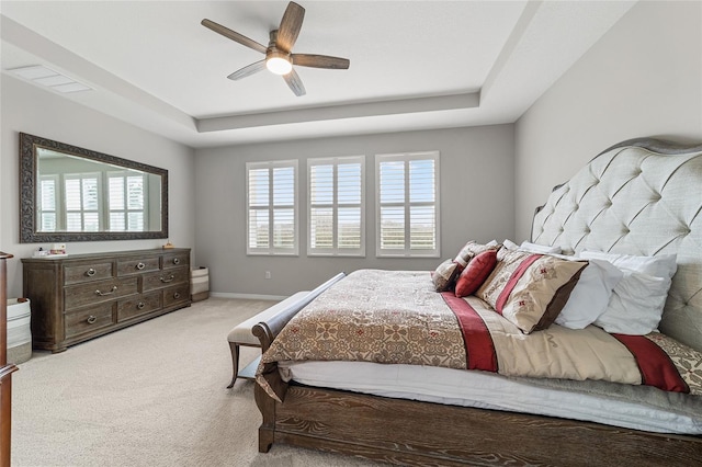 carpeted bedroom with a raised ceiling and ceiling fan