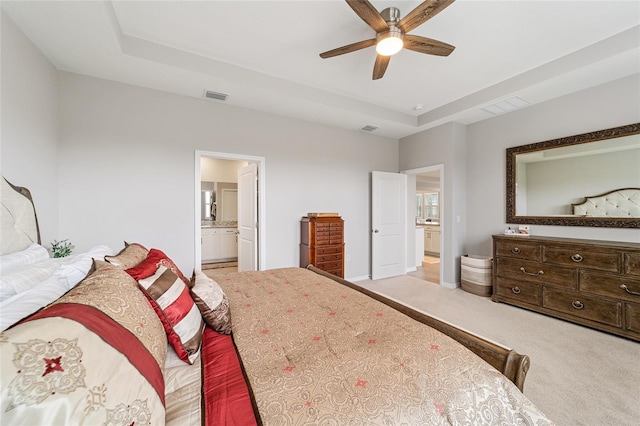 carpeted bedroom with ceiling fan, a tray ceiling, and ensuite bath