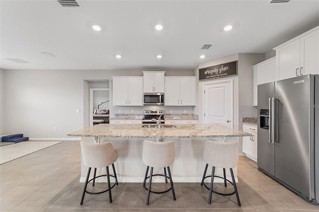 kitchen with white cabinetry, an island with sink, light stone counters, and appliances with stainless steel finishes