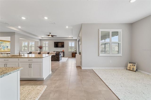 kitchen featuring white cabinets, ceiling fan, a raised ceiling, and light stone counters