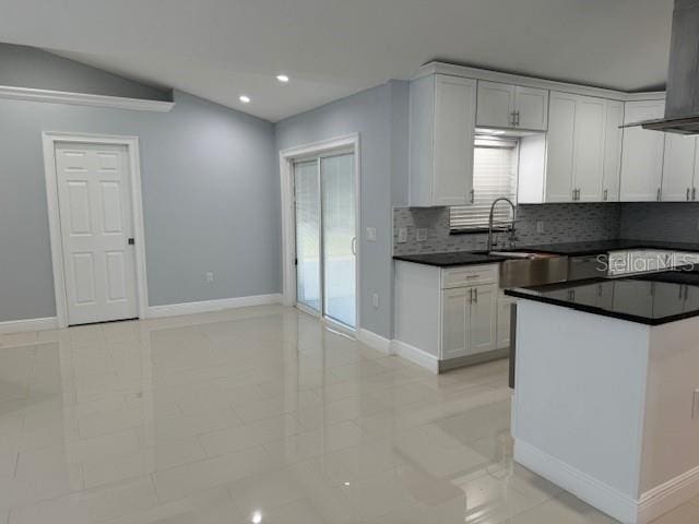 kitchen featuring wall chimney range hood, backsplash, light tile patterned floors, white cabinetry, and sink