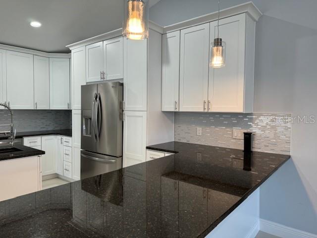 kitchen with stainless steel refrigerator with ice dispenser, dark stone countertops, hanging light fixtures, and backsplash