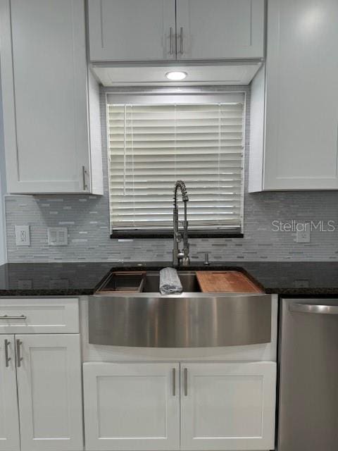 kitchen featuring dishwasher, dark stone counters, sink, white cabinets, and tasteful backsplash