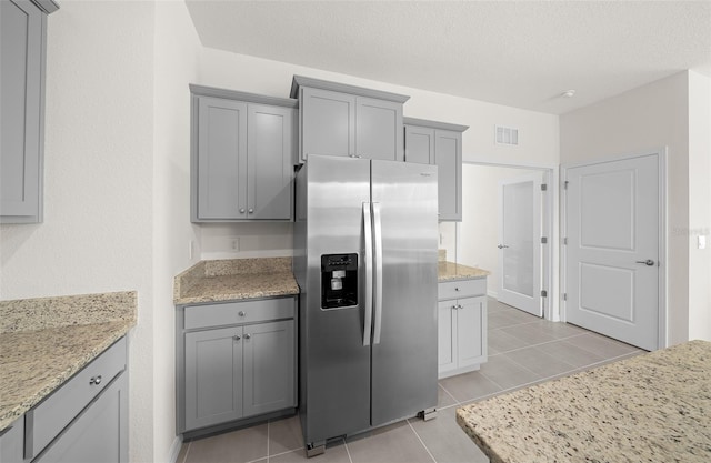 kitchen with stainless steel refrigerator with ice dispenser, light stone counters, and light tile patterned floors