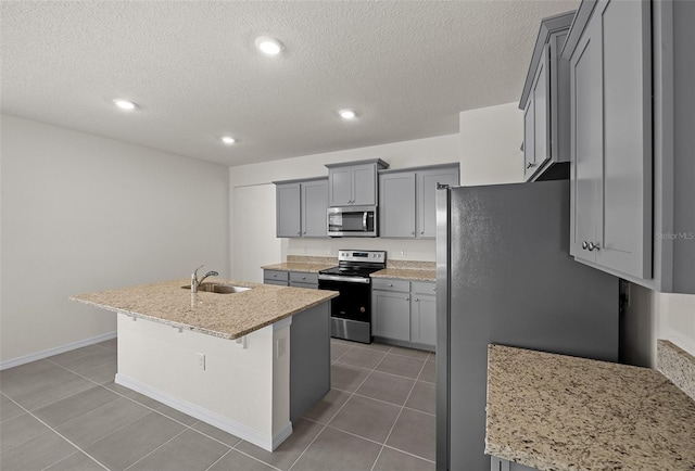 kitchen with stainless steel appliances, an island with sink, sink, gray cabinets, and light stone counters