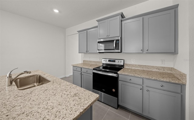 kitchen with light tile patterned floors, appliances with stainless steel finishes, gray cabinetry, light stone countertops, and sink