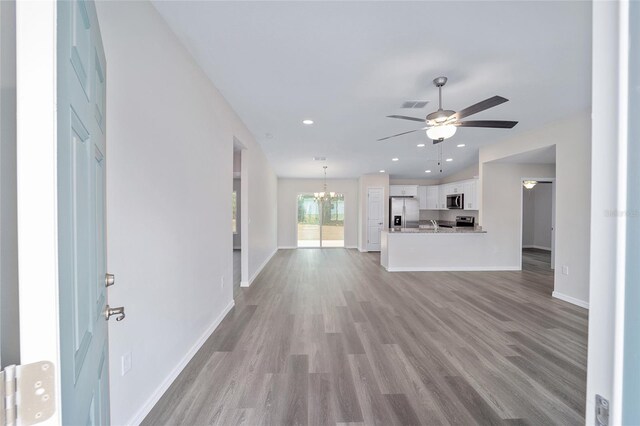 unfurnished living room featuring ceiling fan with notable chandelier and light hardwood / wood-style floors