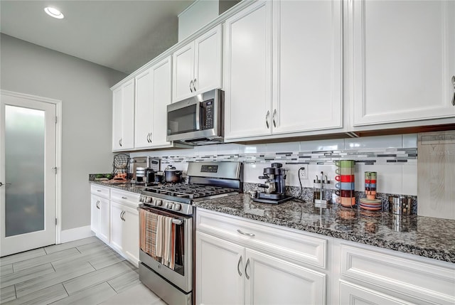 kitchen with white cabinets, dark stone countertops, appliances with stainless steel finishes, and backsplash