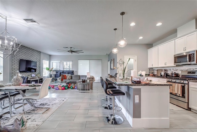 kitchen with a kitchen island with sink, decorative light fixtures, appliances with stainless steel finishes, ceiling fan with notable chandelier, and a kitchen bar