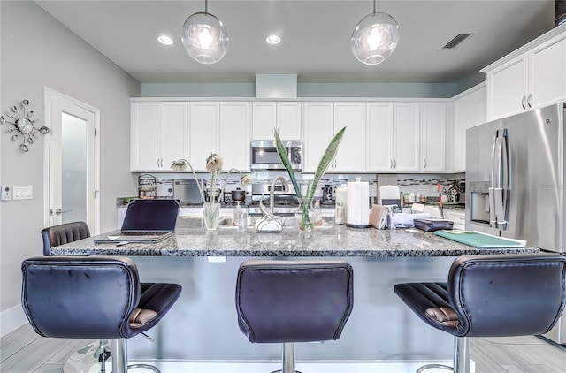 kitchen with a breakfast bar, stainless steel appliances, white cabinetry, and hanging light fixtures