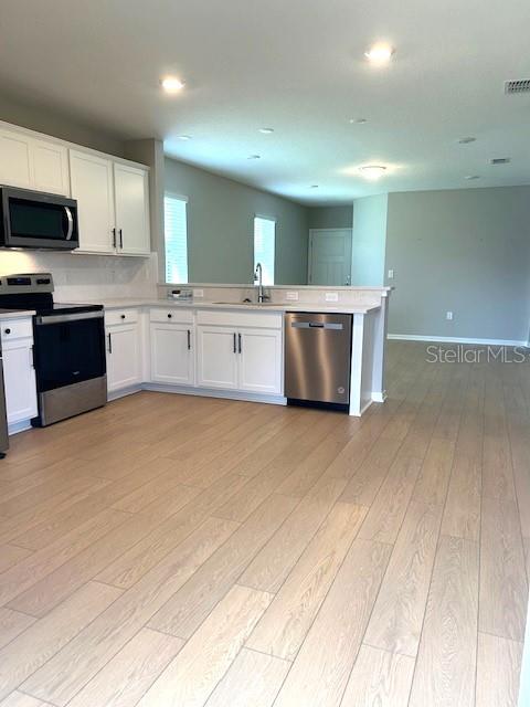 kitchen featuring appliances with stainless steel finishes, light hardwood / wood-style floors, white cabinetry, kitchen peninsula, and sink