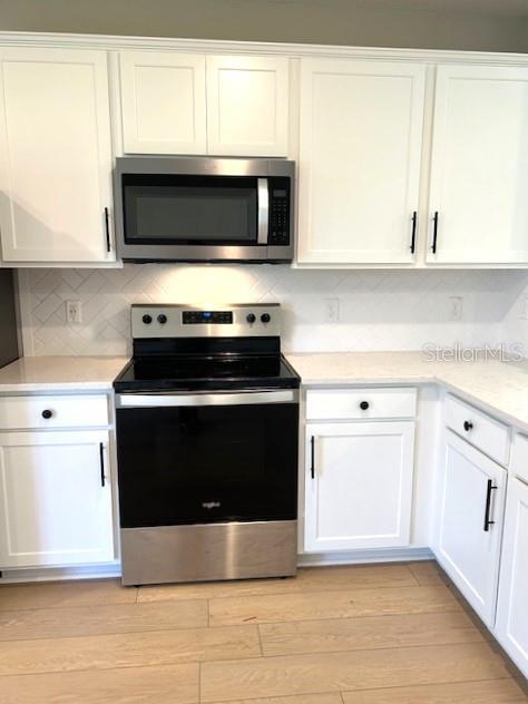 kitchen featuring stainless steel appliances, light hardwood / wood-style floors, tasteful backsplash, and white cabinetry