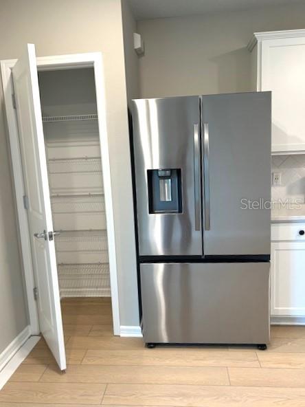 kitchen featuring light hardwood / wood-style floors, stainless steel fridge with ice dispenser, and white cabinetry